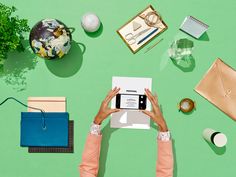 a person holding a cell phone over a desk with various items on it and in front of them