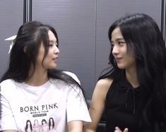 two young women sitting next to each other in front of a locker room door, one with long black hair