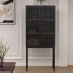 a black cabinet sitting in the middle of a living room next to a vase with flowers