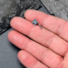 a person's hand holding a tiny ring with a blue flower on it, in front of a stone wall