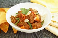 a white bowl filled with meat and veggies on top of rice next to a yellow towel