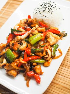 a white plate topped with chicken and veggies next to rice on top of a wooden table