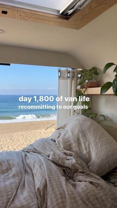 a bed sitting under a window next to the ocean with an advertisement above it that reads day 1, 800 of van life recommating to four goals