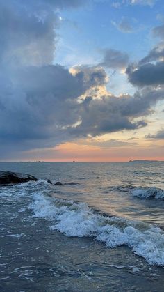 the sun is setting over the ocean with waves crashing on the shore and clouds in the sky