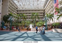 people walking in the lobby of a large building with palm trees and flags hanging from the ceiling