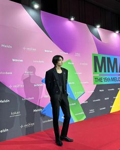 a man standing on top of a red carpet next to a colorful sign that reads mmm