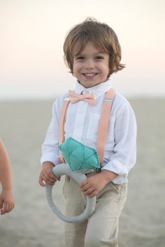 a young boy wearing a bow tie and suspenders holding a toy on the beach