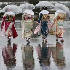 three women walking in the rain with umbrellas over their heads and wearing kimonos