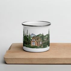 a ceramic mug with a cabin scene on the front is sitting on a wooden surface