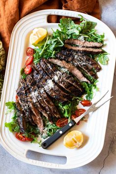 grilled steak with salad and lemon wedges on a platter next to a knife