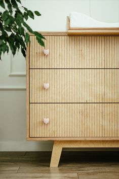 a wooden dresser with knobs on it and a potted plant in the corner