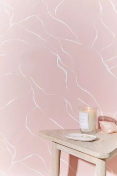 a table with a candle on it in front of a wallpapered pink background