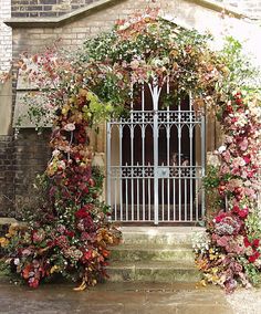 an arch covered in lots of flowers next to a white gate with iron bars on it