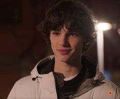 a young man with curly hair wearing a white jacket