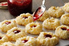 cookies with jam being drizzled onto them and sitting on a baking sheet