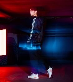 a young man standing in front of a red and blue background wearing adidas shoes