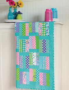 a colorful quilt hanging on the wall next to a vase with flowers and other items