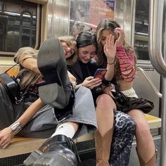 three women sitting on a subway train looking at their cell phones and laughing with each other