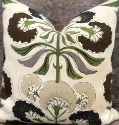 a white pillow with green and brown floral designs on the front, sitting on a wooden surface