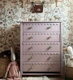 a pink dresser sitting in front of a wallpapered wall next to a stuffed animal