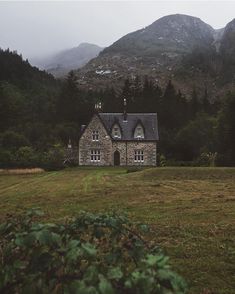 an old stone house in the middle of a field with mountains in the back ground