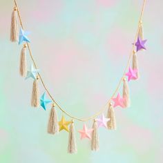 a gold chain with tassels and stars hanging from it's sides on a pastel background