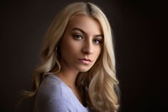 a woman with blonde hair and blue eyes posing for a photo in front of a dark background