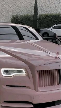 the front end of a pink rolls royce parked in a parking lot next to other cars