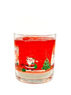 a shot glass filled with red liquid and santa clause on the side, sitting in front of a white background