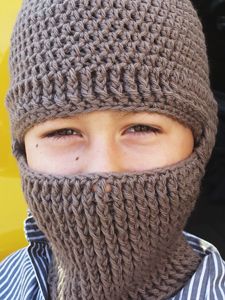 a young boy wearing a knitted hat with a hood on his face and looking at the camera