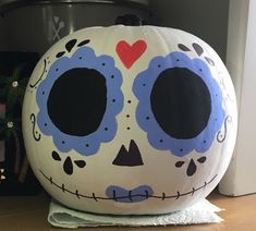 a large white pumpkin decorated with blue and red sugar skull decorations on top of a wooden table