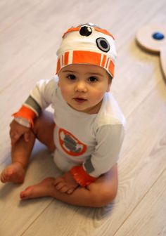 a baby is sitting on the floor wearing a star wars shirt and hat with eyes