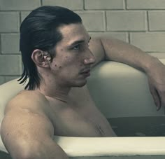 a shirtless man sitting in a bathtub with his arm resting on the edge