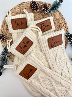 three white knit mitts with brown labels on them and pine cones in the background