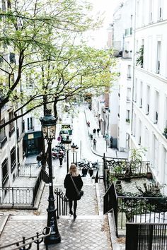 a woman walking down the stairs in an alleyway with trees and buildings on both sides