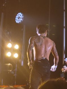 a man with tattoos on his back standing in front of a crowd at a concert