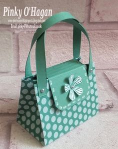 a green and white polka dot bag with a bow on the front, sitting against a brick wall