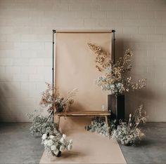 an arrangement of white flowers and greenery in front of a beige backdrop