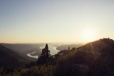 the sun is setting on top of a mountain overlooking a lake and mountains in the distance