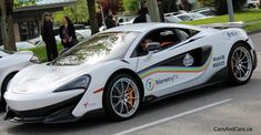 a white sports car parked on the side of the road with people standing around it