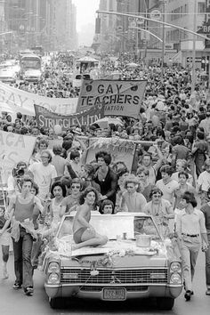 a large group of people marching down the street in a parade with cars and signs