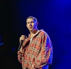 a male in a plaid shirt is holding a microphone and singing into the microphone on stage