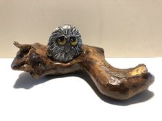 an owl figurine sitting on top of a piece of driftwood next to a wall