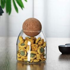 a glass vase filled with yellow flowers on top of a wooden table next to a plant