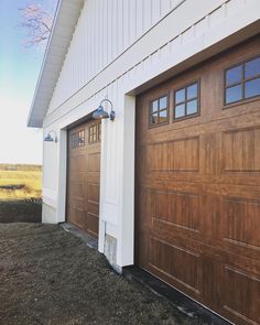 two brown garage doors are open in front of a white building with grass on the ground