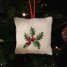 a cross stitch ornament hanging from a christmas tree with red berries on it