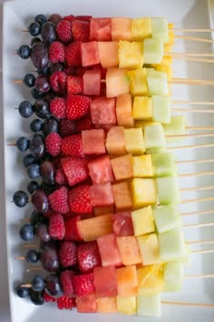 fruit skewers are arranged on a white platter, ready to be eaten