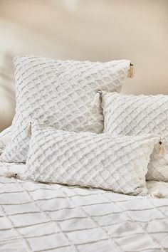 three white pillows sitting on top of a bed next to a pillow with tassels