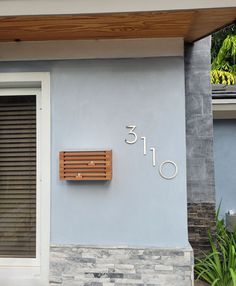 a house number sign on the side of a building with shutters and wood slats