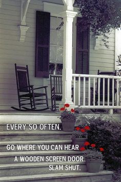 a porch with rocking chairs and flowers on the steps that lead up to an old house